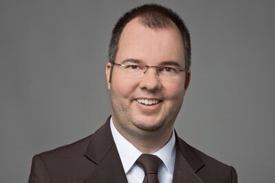 Das Porträt zeigt Andreas Hildenbrand lächelnd vor grauem Hintergrund.