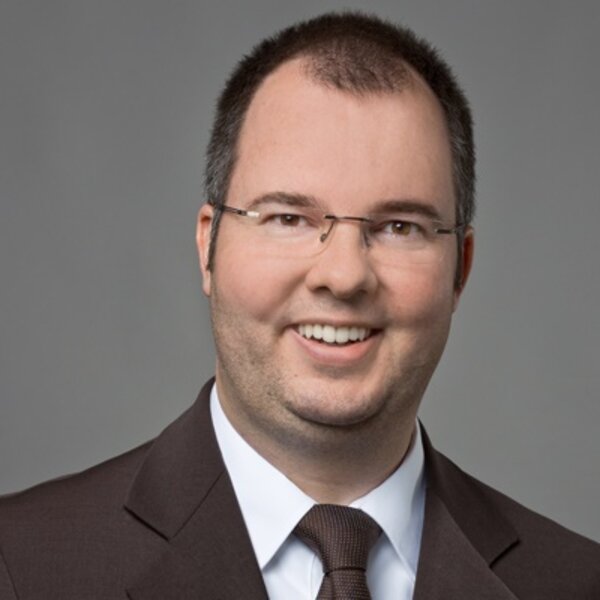 Das Porträt zeigt Andreas Hildenbrand lächelnd vor grauem Hintergrund.