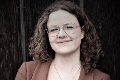 Das Porträt zeigt Angela Nießer lächelnd mit verschränkten Armen vor dunklem Hintergrund.