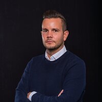Das Porträt zeigt Daniel Schneider mit verschränkten Armen vor dunklem Hintergrund.