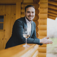 Das Porträt zeigt Sebastian Hill lächelnd in einem Holzblockhaus.