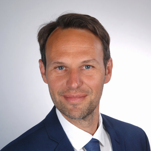 Das Porträt zeigt Michael Hofmann lächelnd vor grauem Hintergrund.