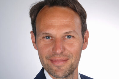 Das Porträt zeigt Michael Hofmann lächelnd vor grauem Hintergrund.